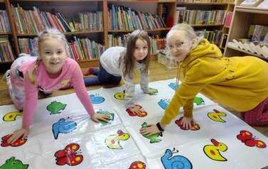 Trzy dziewczynki grają  w rozłożoną na podłodze grę WYGIBAJTUS