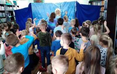 Elza stoi po środku i pokazuje dzieciom ruchy taneczne, a dzieci ją naśladują.