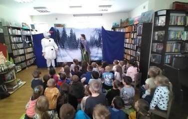 Na tle śnieżnego lasu obok aktorki pojawia sie bałwan Olaf i rozmawiają. Widać dużą publiczność dziecięcą.