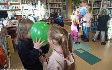 Dzieci tańczą w parach trzymając się za ręce, głowami trzymając wsp&oacute;lnie balonik.