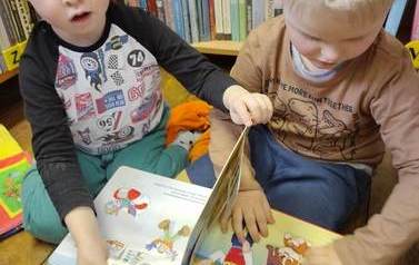 Dw&oacute;ch chłopc&oacute;w siedzi na podłodze i przegląda wsp&oacute;lnie książeczkę.
