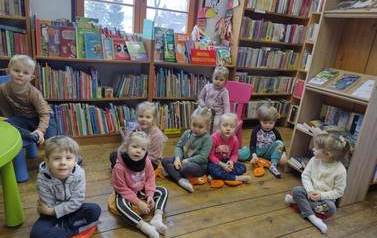 Grupa dzieci siedzących w bibliotece na poduszkach i słuchających bajki.