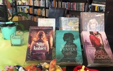 Na stole wystawione są książki o kobietach, cukierki i zwinięte w rulonik aforyzmy do wylosowania.