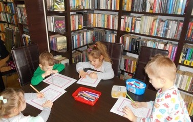 Dzieci przy stoliku kolorują bajkowe obrazki.