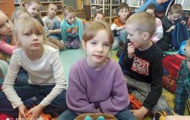 Grupa dzieci siedzących na karimatach i słuchających bibliotekarza.