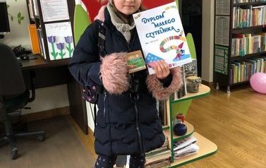 Dziewczynka pokazuje dyplom Małego Czytelnika i kredki.