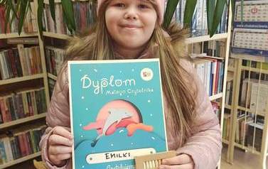 Dziewczynka pokazuje dyplom Małego Czytelnika i kredki.