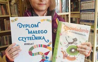 Dziewczynka pokazuje Dyplom i wypożyczoną książkę.