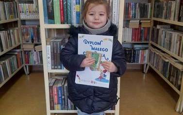 Dziewczynka trzyma w ręku dyplom Małego Czytelnika i kredki.