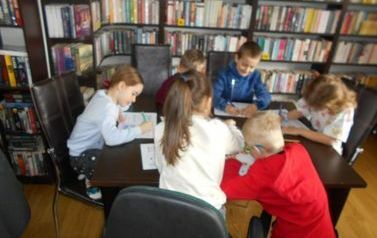 Dzieci siedzą przy stoliku i wykonują powierzone im zadania.