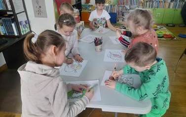 Dzieci stoją przy białym stole i  kolorują postaci z baśni Andersena.