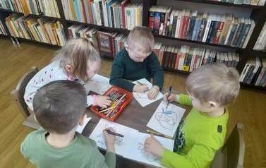 Trzech chłopc&oacute;w i jedna dziewczynka siedzą przy małym stoliku i kolorują obrazki z postaciami z baśni Andresena