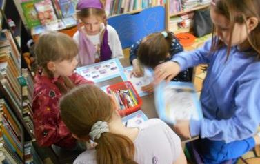 Dziewczynki siedzą przy stoliku i wykonują kartę pracy dotyczącą "Strażaka Sama".