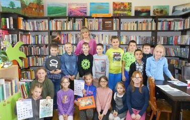 Zdjęcie grupowe dzieci z bibliotekarką, niekt&oacute;re z nich trzymają w ręku swoje karty pracy.
