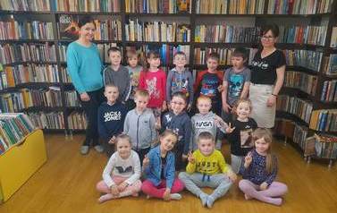 Zdjęcie grupowe dzieci z Panią wychowawczynią i bibliotekarką.W tle p&oacute;łki z książkami.