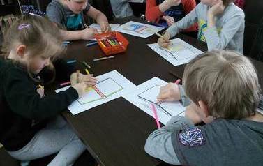 Dzieci siedzą przy stołach i na kartkach projektują okładkę do książki.