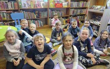Grupa uśmiechniętych dzieci siedzących na siedziskach w Bibliotece.
