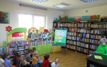 Dzieci siedzą na dywanie, a z prawej strony siedzi zaproszony gość i czyta im bajkę.