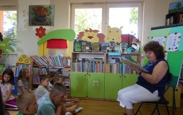 Pani, kt&oacute;ra jest gościem czyta dzieciom bajkę. Dzieci siedzą na dywanie.