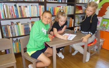 Dwie dziewczynki i chłopiec siedzą przy małym stoliku i robią kartę pracy.