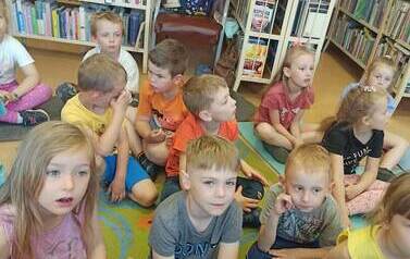 Grupa dzieci siedzi na dywanie i słucha czytanej bajki.