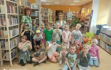 Zdjęcie grupowe dzieci z Panią wychowawczynią i Panią bibliotekarką w bibliotece.