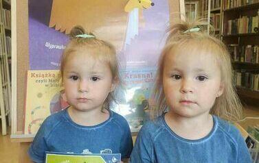 Dwie siostry w niebieskich bluzeczkach pokazują swoje wypożyczone książeczki z serii Kicia Kocia