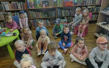 Dzieci siedzą na siedziskach i słuchają bajki czytanej przez Panią z biblioteki.