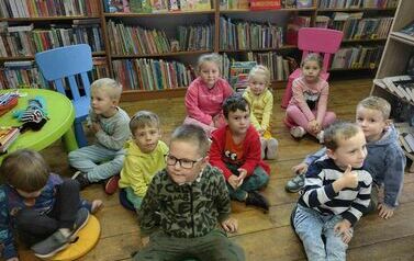 Dzieci siedzą na siedziskach i słuchają bajki czytanej przez bibliotekarkę.