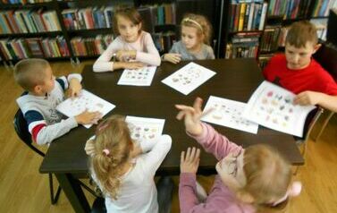 Dzieci przy dużym stole wykonują karty pracy o jesieni.