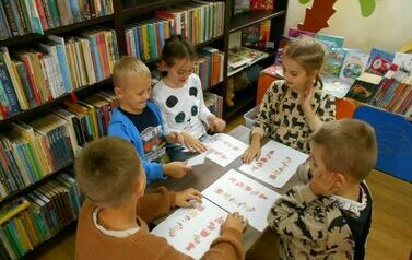 Dzieci siedzą przy małym stoliku i wykonują karty pracy o jesieni.