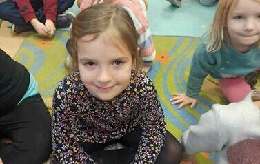 Dzieci siedzą na dywanie i słuchają bajki.