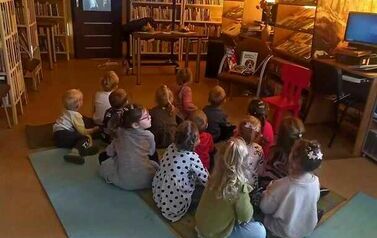 Dzieci siedzą na dywanie i karimatach i oglądają na dużym ekranie film o 1 listopada.