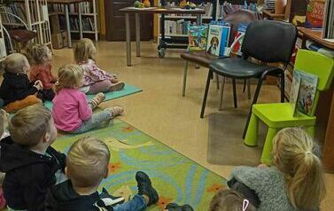 Dzieci siedzą na dywanie i karimatach i oglądają na dużym ekranie film o 1 listopada.