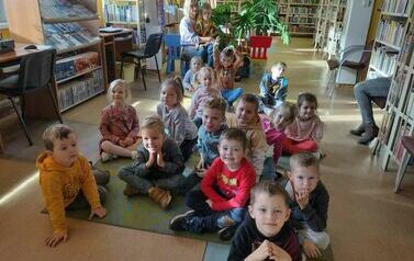 Dzieci siedzą na dywanie i słuchają bajki.