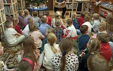Dzieci siedzą na dywanie i patrzą na Szymona G&oacute;ralczyka, kt&oacute;ry im coś opowiada.