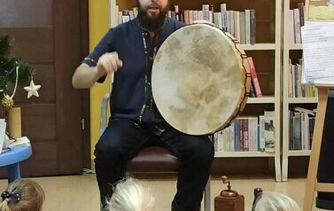 Szymon trzyma na kolanach bęben i coś opowiada dzieciom.