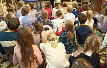 Dzieci siedzą na dywanie i patrzą na Szymona G&oacute;ralczyka, kt&oacute;ry im coś opowiada.