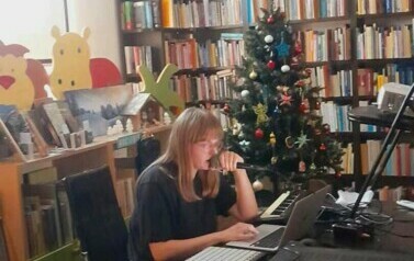 Animatorka siedzi przy stole trzymając mikrofon i sterując sprzętem muzycznym śpiewa r&oacute;żne melodie.