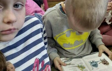 Chłopiec ogląda książeczkę o dinozaurach, obok siedzą inne dzieci.