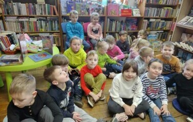 Dzieci siedzą na siedziskach i słuchają czytanej bajki przez bibliotekarkę.