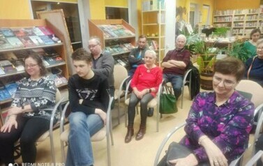 Na krzesłach w bibliotece siedzą czytelnicy.