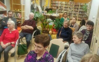 Na krzesłach w bibliotece siedzą czytelnicy.