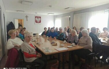 Przy stołach siedzą emeryci przy kawie i ciastkach i patrzą na występ Szymona G&oacute;ralczyka.