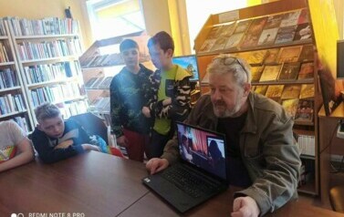 Piotr Martin przy stole pokazuje młodzieży jakieś nagranie z laptopa.