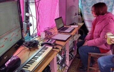 W busie przy laptopie siedzi dziewczyna, a obok słabo widoczna Iwona Skwarek. Widać sprzęt muzyczny w busie.