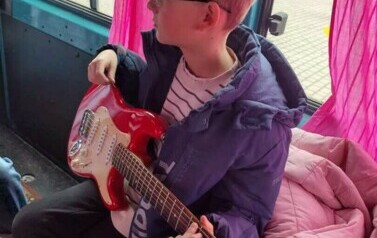 W busie siedzi chłopiec z gitarą elektryczną.