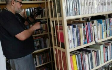 Pomiędzy regałami w bibliotece jest schowany Piotr Martin z kamerką.