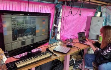 Przy sprzęcie muzycznym w busie siedzi Iwona Skwarek. Widać laptopa, głosniki, klawisze, duży monitor, mikrofony i inne wytwory muzyczne.