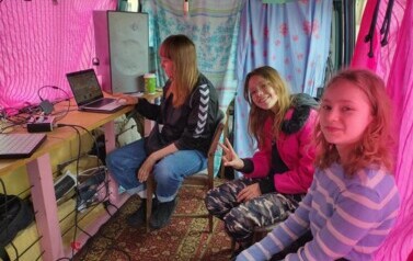 W busie przy laptopie siedzi Iwona, a obok siedzą dwie uśmiechnięte dziewczynki.